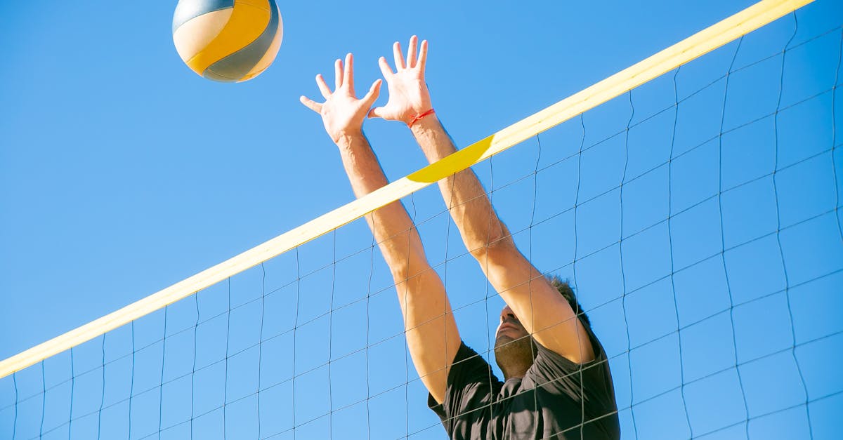 Dynamic outdoor volleyball game with a male player blocking a ball under clear blue skies.