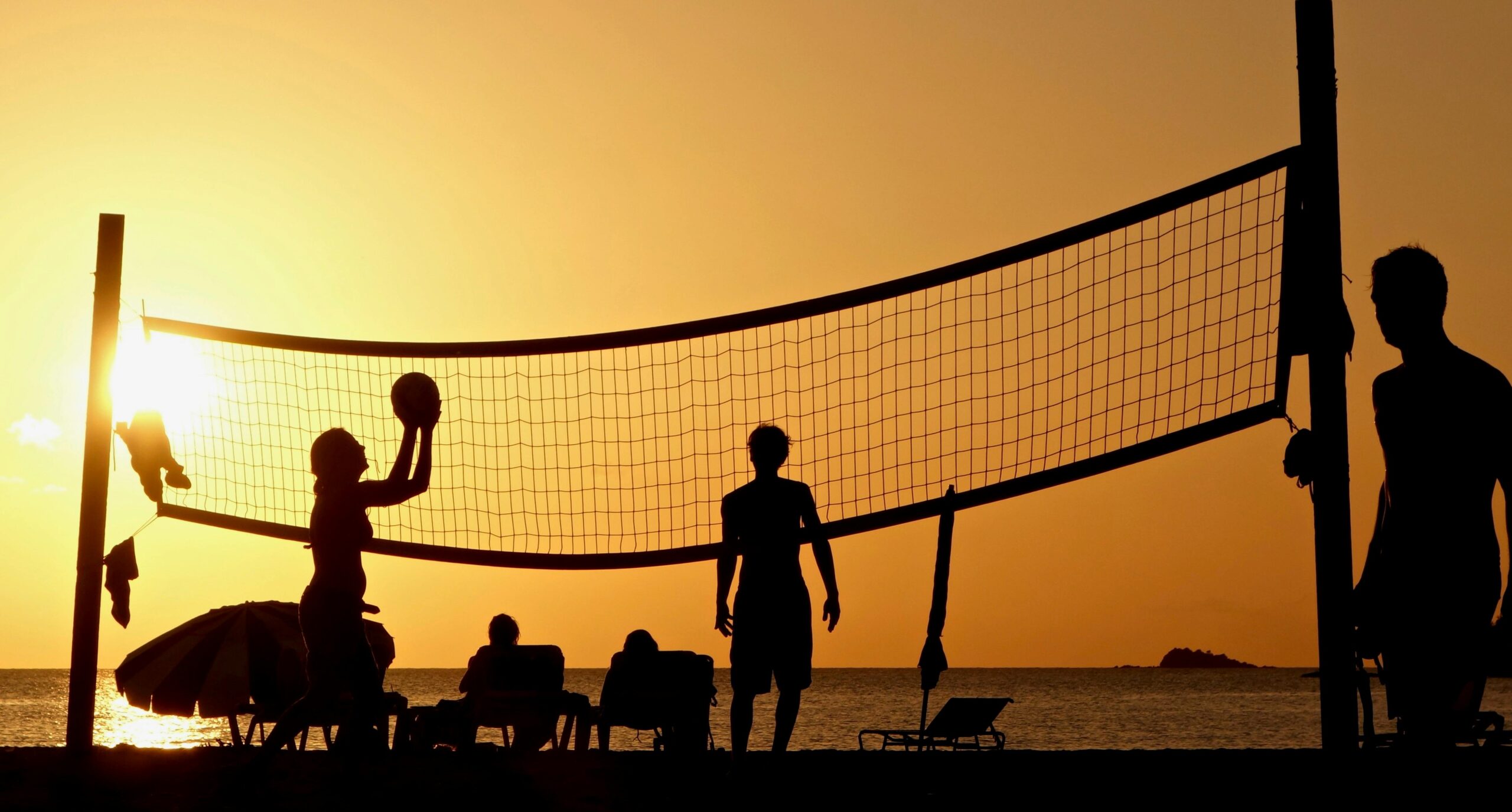 Silhouettes playing volleyball on Antigua's beach during a warm sunset.